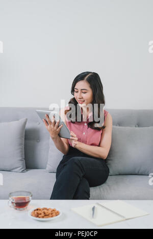 Asiatische Frau auf der Couch zu Hause online shopping, so bequem, in fashioanble weißen Outfit, so schönes Licht design interieur Innen Stockfoto