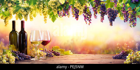 Flaschen und Weingläser mit Trauben bei Sonnenuntergang Stockfoto