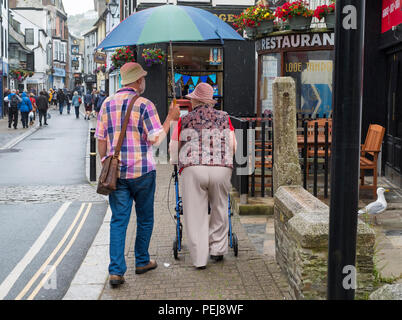 Älterer Mann und Frau gehen mit Dach entlang einer Straße in Looe, Cornwall, England, Großbritannien Stockfoto