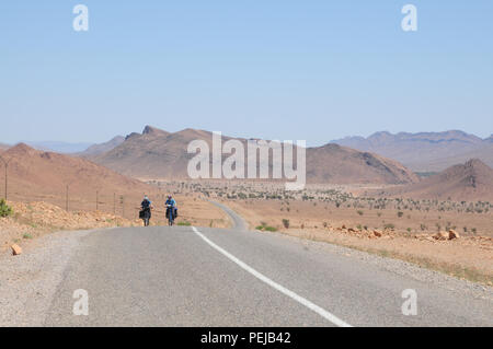 Zwei Radfahrer machen sich auf den Weg entlang einer Straße am Rande der Sahara in Marokko, Position zwischen Tata und igherm am Rande des Anti Atlas Gebirge. Stockfoto
