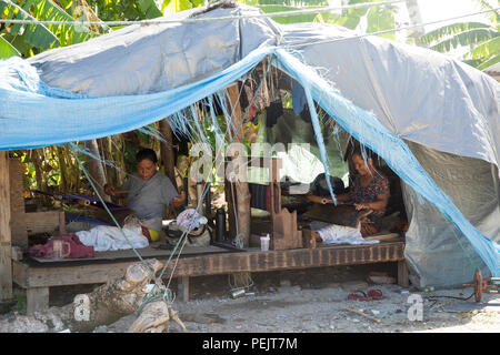 Frauen arbeiten am 7. Dezember 2015 an Reparaturen in einem mit einer Plastikplane bedeckten Haus auf Falalop Island im Ulithi Atoll, Föderierte Staaten von Mikronesien. Die Gemeinde erholt sich weiter vom Taifun Maysak, der im März 2015 direkt über das Atoll zog und viele Strukturen und beschädigte Infrastruktur zerstörte. Die Kunststoffplane schützt die Wohnung vor Witterungseinflüssen, da der Wiederaufbau voranschreitet und die Bewohner sich mit Dach- und Wandreparaturen befassen. Stockfoto
