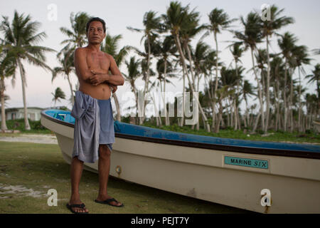 Ein Fischer steht neben seinem Boot auf Falalop Island, Ulithi Atoll, FSM, und folgt dem Taifun Maysak, der mit 160 km/h Winden zuschlug und erhebliche Schäden an Vegetation, Strukturen und Vorräten über das Atoll verursachte. Die Szene zeigt die Anfälligkeit der Inselgemeinden für Taifune der Kategorie 5. Die Operation Christmas Drop 2015 beinhaltete humanitäre Hilfe und Ausbildungsmaßnahmen in der Region, wobei die Bemühungen des Personals der USAF, des JASDF und der RAAF, das in Yokota ab und Andersen AFB stationiert war, einbezogen wurden. Stockfoto
