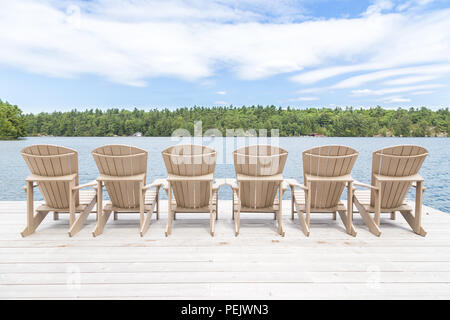 Reihe von Muskoka Stühle auf ein Dock mit Blick auf den See. Stockfoto