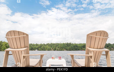 Muskoka Stühlen, mit Blick auf den See und eine Schale mit Kirschen und ein Glas Champagner. Stockfoto