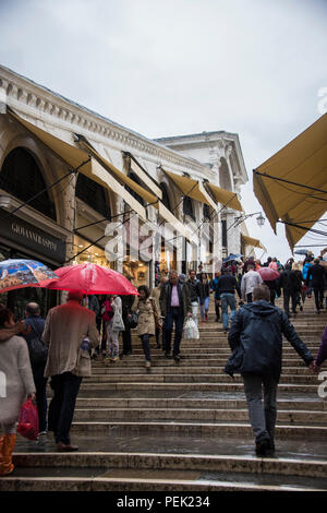 Betrachten Sie die Schritte von der Rialto Brücke über den Canal Grande, mit Geschäften und Touristen im Regen, Venedig Stockfoto