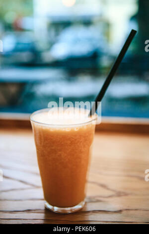 Frisch gepresster Orangensaft in ein Glas mit Strohhalm auf dem Tisch in einem Cafe neben dem Fenster. Nützliche Morgen trinken. Stockfoto