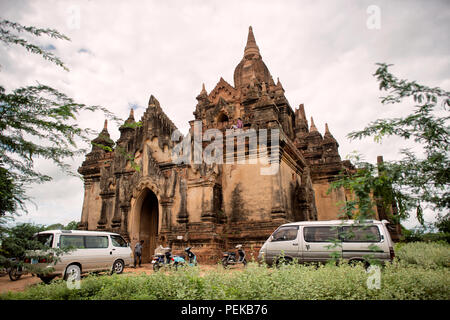 Thisa-Wadi-Tempel Bagan Myanmar // BAGAN, Myanmar — Vans und Motorräder parken vor dem Thisa-Wadi-Tempel (auch bekannt als Thissa-Wadi-Tempel) und bringen Touristen zu diesem buddhistischen Denkmal aus dem 14. Jahrhundert in der archäologischen Zone Bagan. Nach epigraphischen Beweisen aus dem Jahr 1334 wurde der dreistöckige Tempel in der postkaiserlichen Zeit errichtet, fast ein halbes Jahrhundert nach dem Fall des heidnischen Königreichs. Der Tempel ist bei Besuchern als eines der wenigen Denkmäler in Bagan populär geworden, wo das Klettern auf die oberen Terrassen erlaubt ist und einen Panoramablick über das antike Tempelgebiet bietet Stockfoto