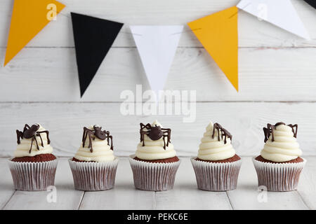 Halloween Cupcakes mit Schokolade Spinnen in einer Reihe auf Holzbohlen mit festlichen Orange, Schwarz und Weiß Girlande Stockfoto