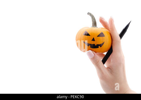 Woman's Hand, die kleine bemalt Halloween Kürbis und schwarzen Filzstift auf weißem Hintergrund. Urlaub Dekoration Konzept. Stockfoto