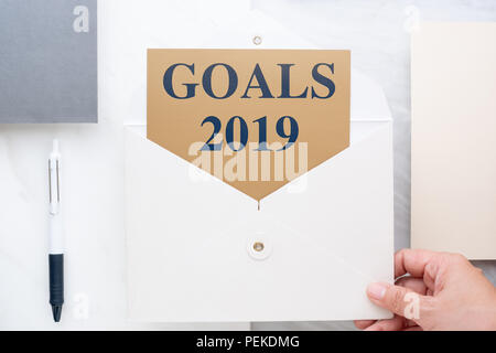 Blick von oben auf die Hand, die weißen Briefumschlag mit Ziele 2019 die Vorsätze im Neuen Jahr auf Gold Karte im Umschlag mit Papier und Stift Marmortisch Büro Schreibtisch. Fut Stockfoto