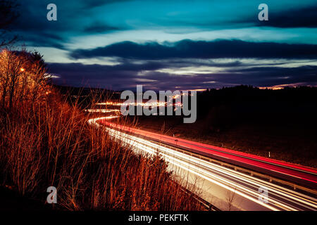 Lange Belichtung Night Shot einer Autobahn aus der Region Freiburg in der Schweiz, mit weißen Fahrzeug leichte Wanderwege und der öffentlichen Beleuchtung Stockfoto