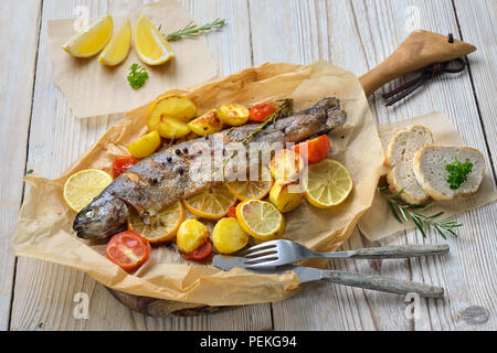 Gebackene Zitrone Forellen mit Backofen - geröstete Rosmarin Kartoffeln und Tomaten, auf Backpapier serviert. Stockfoto