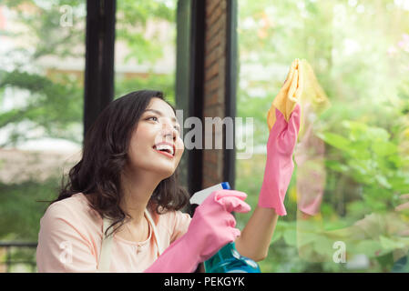 Lächelnde junge Asiatin Hausfrau wäscht ein Fenster Stockfoto