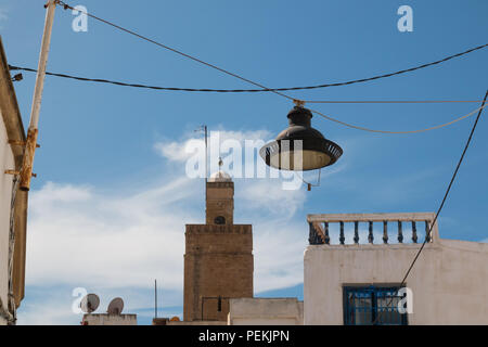 Straßenlaterne hängen auf der Kabel zwischen den Häusern. Traditionelle Architektur und Minarett einer Moschee im Hintergrund. Bewölkter Himmel. Rabat, Marokko. Stockfoto