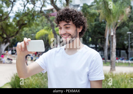 Kaukasische junger erwachsener Mann mit Bart Fernsehen mit Handy Outdoor im Sommer Stockfoto