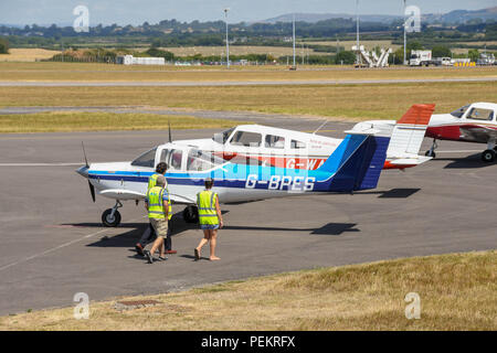 Menschen in Warnwesten vorbei gehen eine Reihe von leichten Flugzeugen in Cardiff Wales Flughafen geparkt. Stockfoto