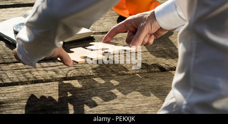 Ansicht von hinten In der Nähe der Hände eines Mannes zusammen zwei komplementäre puzzle Stücke auf einem rustikalen Holztisch im Freien in der Sonne. Stockfoto