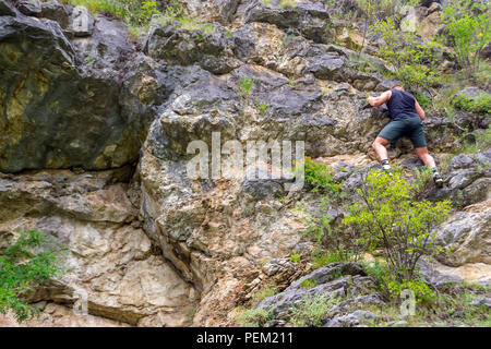 Junger Mann Bergsteiger in Sport Kleidung klettert auf Felsen nach oben in den Bergen der Altai ohne Ausrüstung und Versicherung Stockfoto