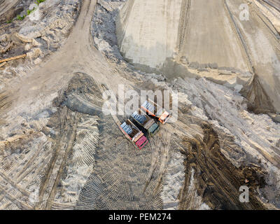 Antenne Blick von oben auf die drei Tipp Nutzfahrzeuge neben einander Warten auf Laden von Sand und Erde auf einer Baustelle mit einer Sand Oberfläche und einem Cou Stockfoto