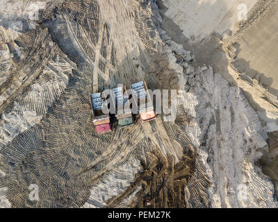 Antenne Blick von oben auf die drei Tipp Nutzfahrzeuge neben einander Warten auf Laden von Sand und Erde auf einer Baustelle mit einer Sand Oberfläche und einem Cou Stockfoto