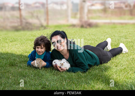 Mutter und Sohn kleine Kaninchen und sitzen gemeinsam auf Gras Stockfoto