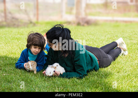 Mutter und Sohn Festlegung auf Gras, kleine Hasen und Gespräch Stockfoto