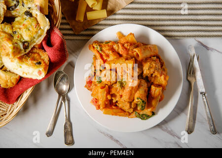 Cremiger italienischer Tomatensoße Rigatoni mit würzigen Würstchen und Seite der käsigen Olivenöl Knoblauch Brot Stockfoto