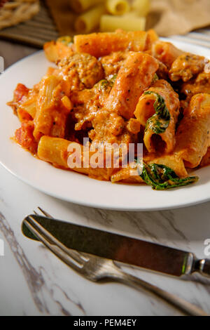 Cremiger italienischer Tomatensoße Rigatoni mit würzigen Würstchen und Seite der käsigen Olivenöl Knoblauch Brot Stockfoto