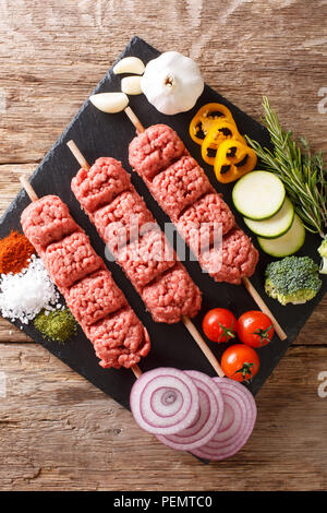 Hausgemachte Kebabs aus rohem Hackfleisch auf Spieße mit Gewürzen, Kräutern und Gemüse close-up auf den Tisch. Vertikal oben Ansicht von oben Stockfoto