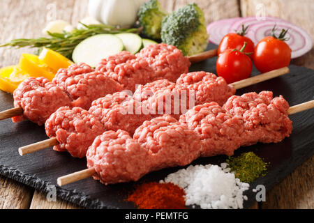 Vorbereitet raw Kebab aus Hackfleisch/Faschiertem auf Spieße mit Zutaten und Gemüse close-up auf dem Tisch. Horizontale Stockfoto