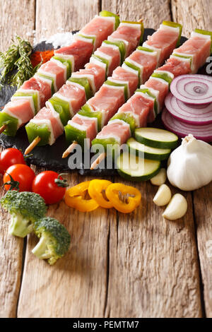 Bereit, roh marinierte Schweinefleisch Shish Kebab mit Pfeffer auf Spieße close-up und Zutaten, Gemüse, Gewürze, Kräuter auf dem Tisch. Vertikale Stockfoto