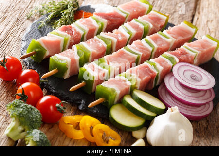 Vorbereitung der Grill: raw Shish Kebab mit grünem Pfeffer auf Spieße close-up und Gemüse, Kräuter auf dem Tisch. Horizontale Stockfoto