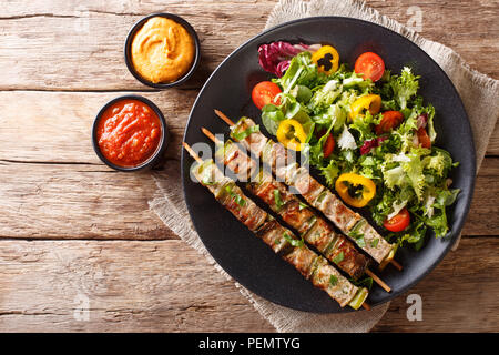 Würzigem Schweinefleisch Shish Kebab mit grünem Pfeffer auf Spieße mit frischem Salat auf einen Teller und Saucen close-up auf einem Tisch. Horizontal oben Ansicht von oben Stockfoto