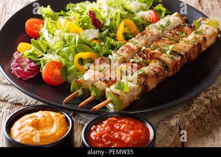 Grill Kebab mit Gemüse auf Spieße mit frischem Salat auf einen Teller und Saucen close-up auf einem Tisch. Horizontale Stockfoto