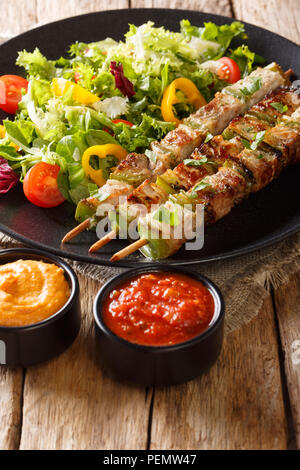 Hausgemachte rustikalen Shish Kebab am Spieß mit Gemüse, frischen Salat auf einen Teller und Saucen close-up auf einem Tisch. Vertikale Stockfoto