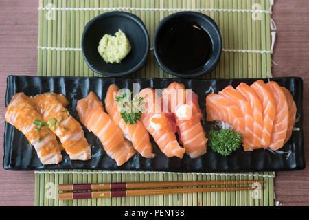 Gemischte lachs Sushi auf schwarze Platte zusammen mit japanischen Sauce und green leaf Dekoration, Japanisch essen, Topview im Sushi. Stockfoto