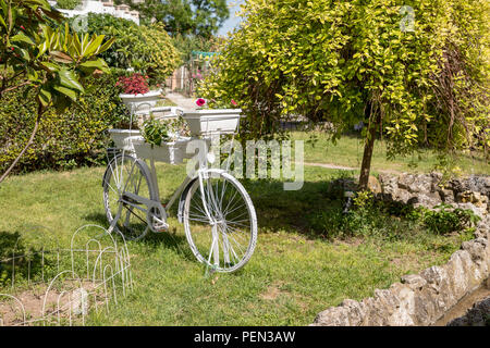 Vintage White Fahrrad mit Körbe mit Blumen im Garten. Schöne Dekoration auf einem natürlichen Hintergrund Stockfoto