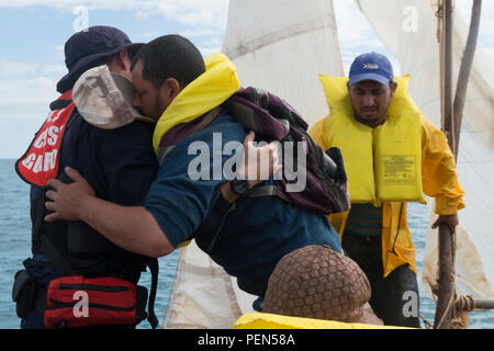 Coast Guard Petty Officer 1st Class Jorge Canedo, einem zertifizierten Spanisch Dolmetscher und Crewmitglied an Bord der Coast Guard Cutter Kathleen Moore, unterstützt eine Kubanische Mann an einem kleinen Boot der Küstenwache im Karibischen Meer, Dez. 9, 2015. Im Laufe von drei Tagen die Crew der Kathleen Moore untersagt 50 kubanischen Migranten angeblich versucht, die in den USA illegal. (U.S. Coast Guard Foto von Petty Officer 3. Klasse Ashley J. Johnson) Stockfoto