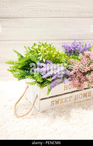 Blumen in einem weißen Holzkiste. Inneneinrichtung, Interieur Komposition. Blumen und Zweige in einer Holzkiste auf weißem Holz- Hintergrund Stockfoto