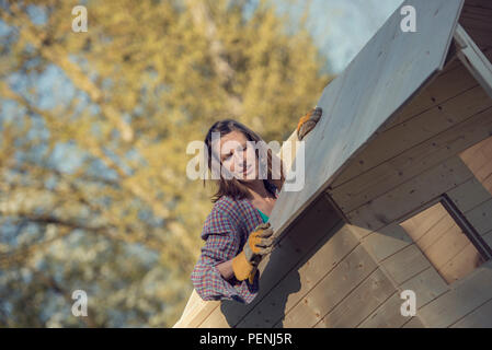 Frau in T-Shirt, ein Holzbrett auf dem Dach von Gartenhaus, ein Do-it-yourself-Bau, getönten retro Effekt. Stockfoto