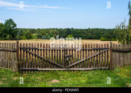 Geschlossen alte hölzerne farm Gate. Hinter dem Feld und Wald. Stockfoto