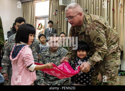 Während ein Staffellauf durchgeführt Dez. 2, 2015, in der Heiligen Familie zu Hause in Osaka, Japan, zwei junge Damen helfen Armee Sgt. Maj. Danny Sanders, ein Oceanside, Kalifornien, native als G3 (Pläne und Operationen) Sergeant Major, U.S. Army Japan (USARJ), Balance eine Kugel auf ein Taschentuch zu dienen. Das Spiel war eines von mehreren interaktiven Aktivitäten der US-Armee in Japan und Japan Masse Verteidigung-kraft (JGSDF) Mittlere Armee senior Unteroffiziere führte eine engere Verbindung mit der Heiligen Familie Home Kinder, freiwillige Helfer und Mitarbeiter zu entwickeln. Heilige Familie Beziehung mit den USA Ar Stockfoto