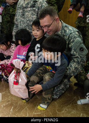 Kinder der Heiligen Familie zu Hause sitzen auf dem Schoß von Armee Sgt. Maj. Michael I. Bair, Senior Berater für US-Soldaten der Armee von Japan (USARJ) Kaplan abschnitt, während eines bilateralen Urlaub Besuch dieser historischen Waisenhaus in Osaka, Japan, Dez. 2, 2015. Bair und Service Mitglieder aus USARJ und der japanischen Boden Verteidigung-kraft half den Kindern, freiwillige Helfer und Mitarbeiter der Heiligen Familie die Feiertage mit Musik, Spielen und Geschenken feiern. Beziehung heiligen Familie zu Hause mit der US-Armee begann Weihnachten 1949, als Soldaten aus dem 27 Infanterie Regiment, besser bekannt als The Wolfhounds Stockfoto