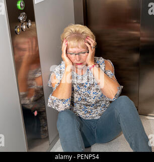 Ältere Frau im Aufzug stecken geblieben. Sitzt auf dem Hochheben, warten auf Hilfe und Rettung Stockfoto