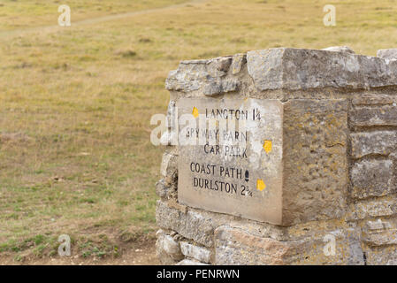 Entfernungen Zeichen geschnitzt in ein großes Stück Stein am Ende einer Wand auf der South West Coastal Path auf Langton, Dorset, England, Großbritannien Stockfoto