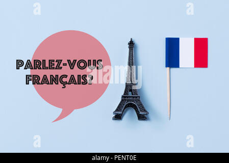 Eine Miniatur des Eiffel Turm, eine Flagge Frankreichs und die Frage Parlez-vous Francaise, haben sie Französisch sprechen? In französischer Sprache geschrieben, gegen eine off-white Stockfoto