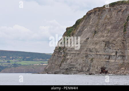 Klippe an der Küste in der Nähe von Robin Hood's Bay, North Yorkshire, England, UK, mit Resten der Trawler, Sarb J, ruiniert in den 1980er Jahren. Stockfoto