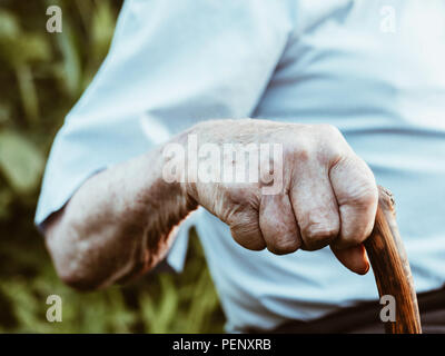 Faltigen Hände alte Mann' auf dem Stick gekreuzt. Nahaufnahme einer nachdenklich Großvater sitzt alleine im Freien und ruht auf einem Stock. Stockfoto