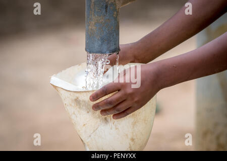 Kleine Hände halten einen Trichter, so dass ein wasserkrug von einer Pumpe in Ganta gefüllt werden kann, Liberia Stockfoto