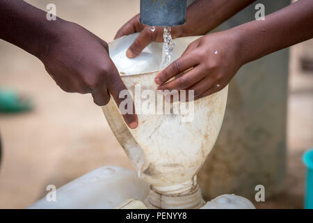 Kleine Hände halten einen Trichter, so dass ein wasserkrug von einer Pumpe in Ganta gefüllt werden kann, Liberia Stockfoto